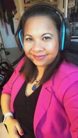 Rowena at desk with headphones and pink blazer